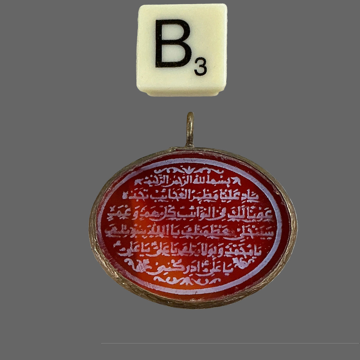 Medallion with Arabic text on a textured surface with a letter 'B' tile.